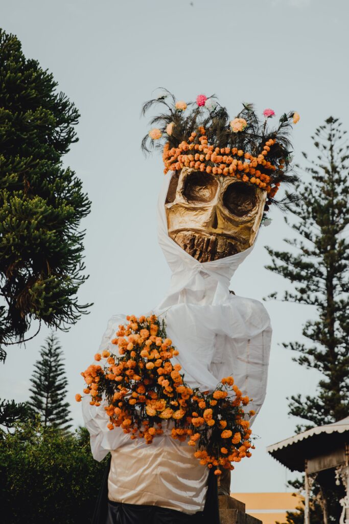 A vertical shot of a large wooden skeleton sculpture with flowers for the La Catrina holiday flor de cempasúchil