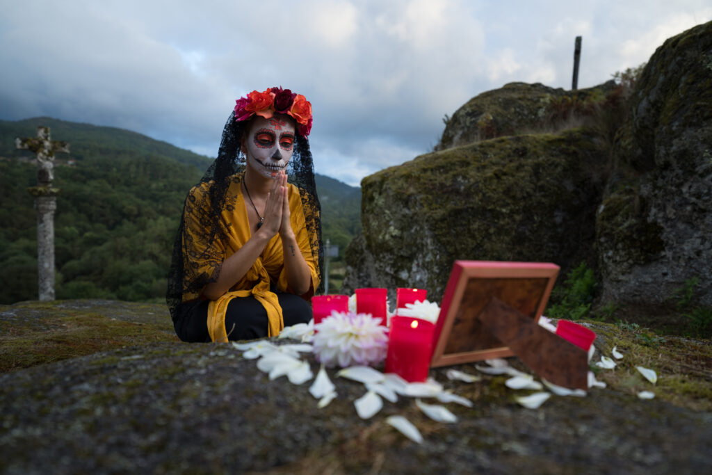 Woman celebrating day of the dead praying in front of grave flor de cempasúchil