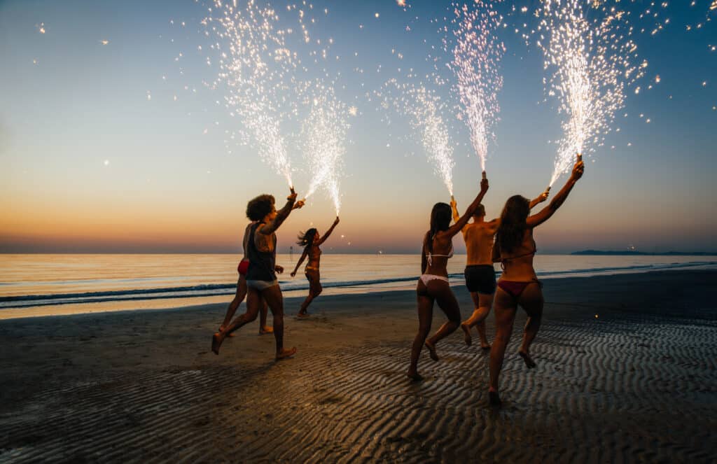 Group of friends having fun running on the beach with sparklers Destinos para celebrar año nuevo